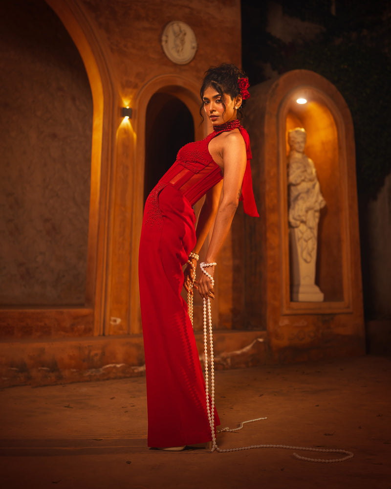 ISHQe campaign: red halter neck gown in side profile beside a stone statue