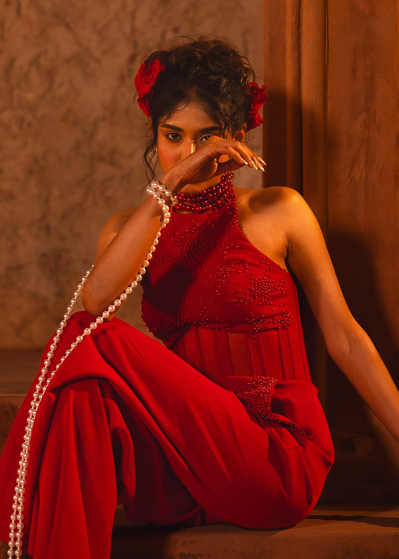 ISHQe campaign: model seated in a red halter neck jumpsuit holding pearl strands