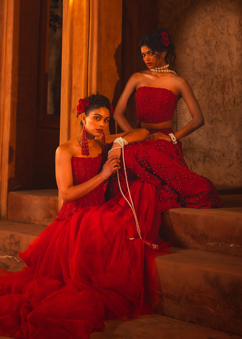 ISHQe campaign: two models in red corset lehengas seated on stone steps with pearl strands