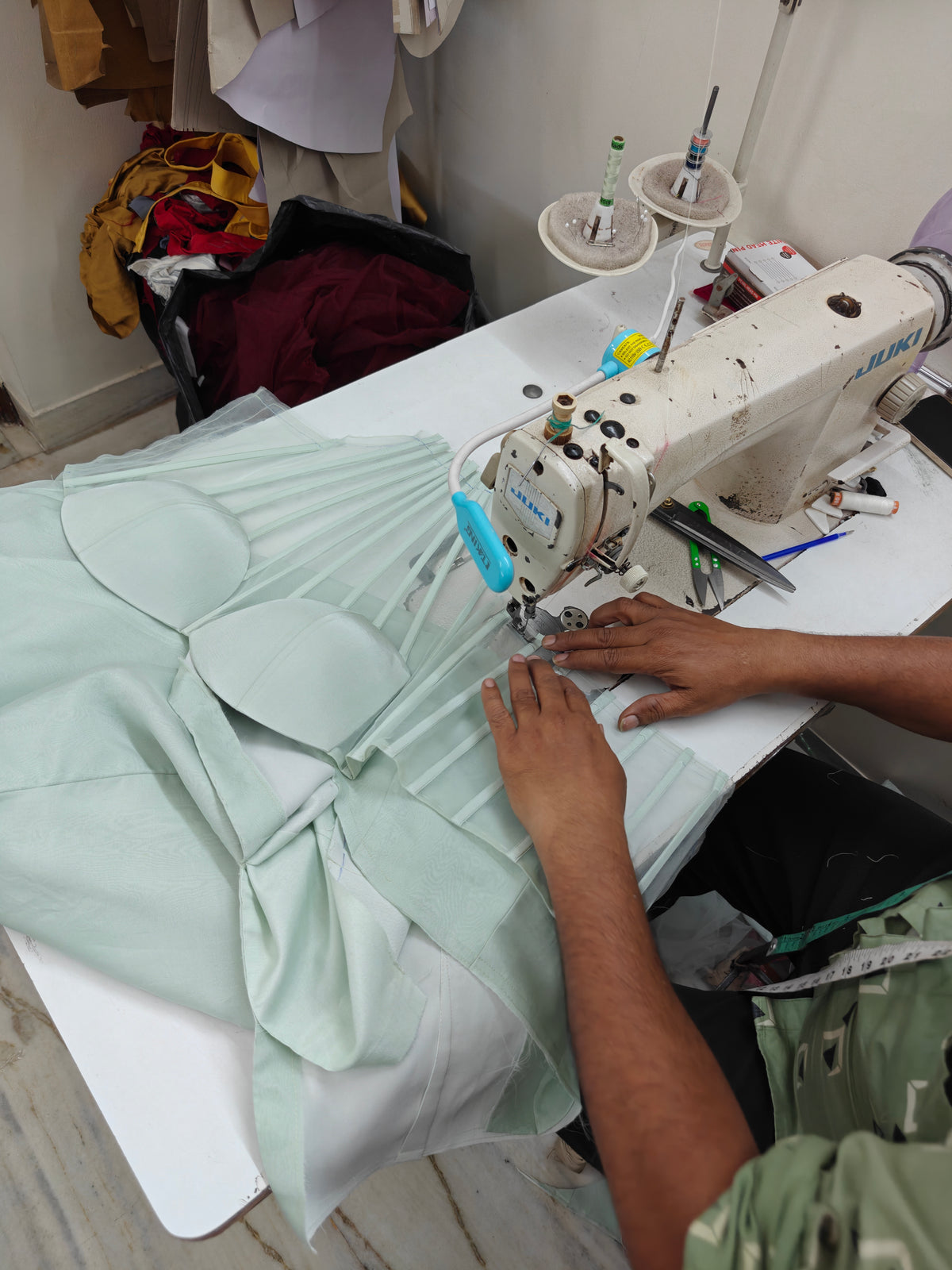 Tailor stitching mint green pleated panels on a sewing machine in the studio