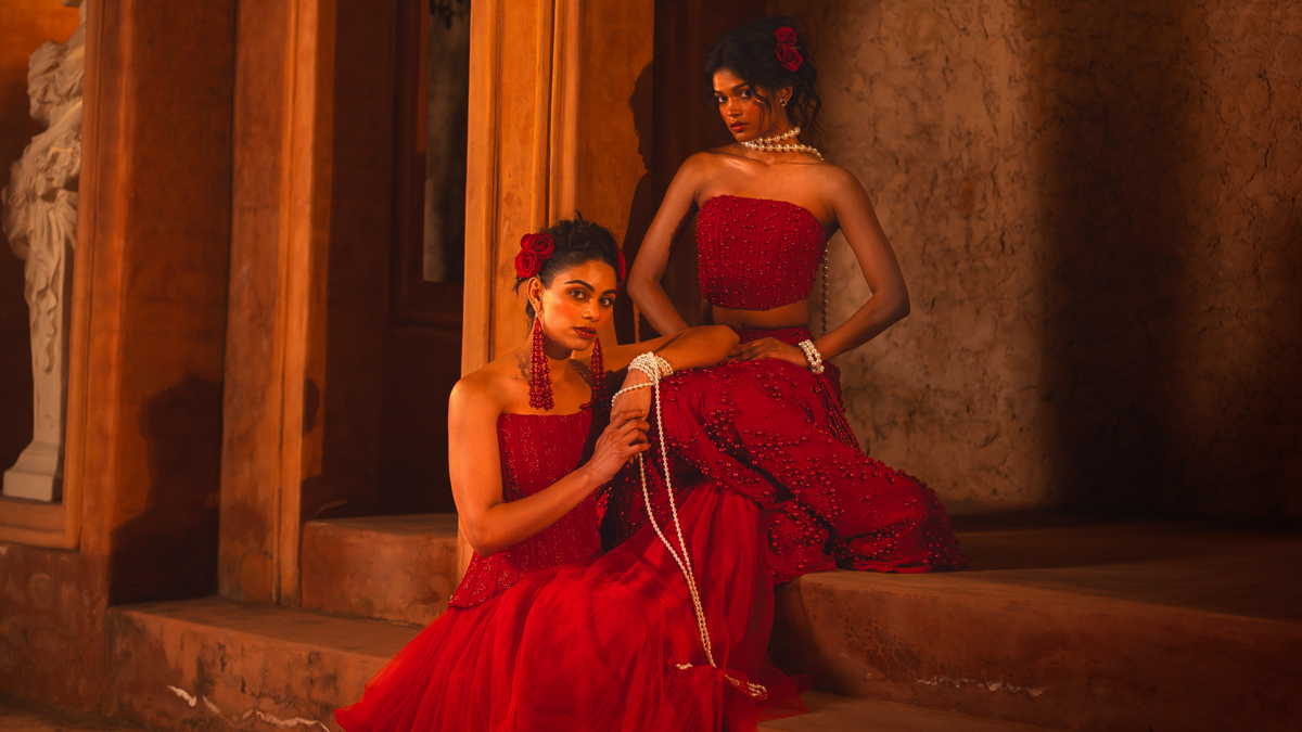 ISHQe collection: two models in red corset lehengas threading pearls on stone steps